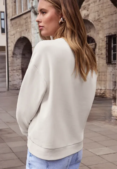 Frau von hinten in weißem Sweatshirt und Jeans vor historischem Steinbau.