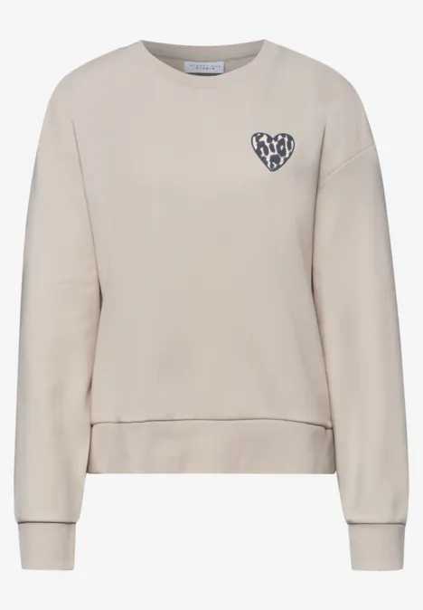Beiges Sweatshirt mit Rundhalsausschnitt, langen Ärmeln und kleinem Herz-Patch auf der Brust.