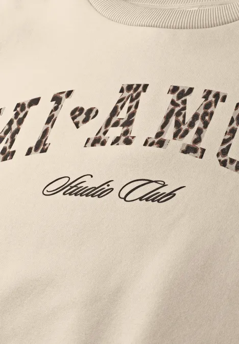 Beiger T-Shirt-Ausschnitt mit Leopardenmuster-Print 'MI-AMU' und darunter Schriftzug 'Studio Club'.
