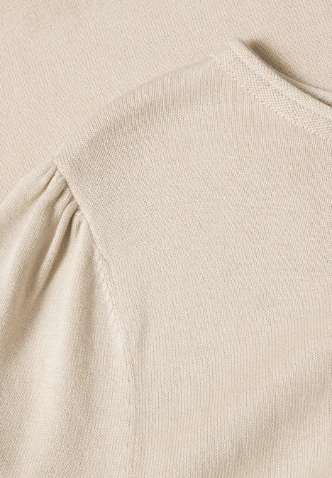 Beige Strickoberteil mit gerafftem Puffärmel in Nahaufnahme.