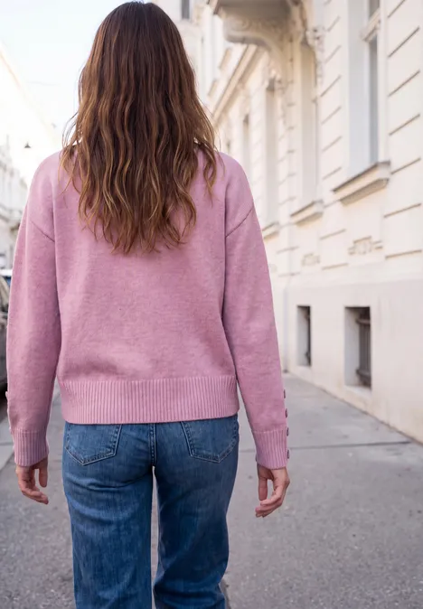 Eine Frau mit rosa Pullover und Jeans geht auf einem Bürgersteig entlang