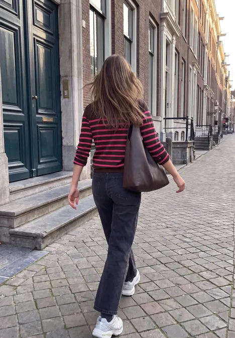Pullover mit Turtle Neck und Streifen russet red Eine Frau in rot-schwarzem Shirt und schwarzer Hose läuft auf Kopfsteinpflaster an Häusern vorbei.