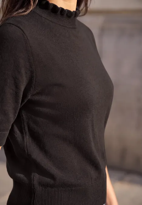 Nahaufnahme einer Person in schwarzem Kurzarm-Strickshirt mit Rüschenkragen.