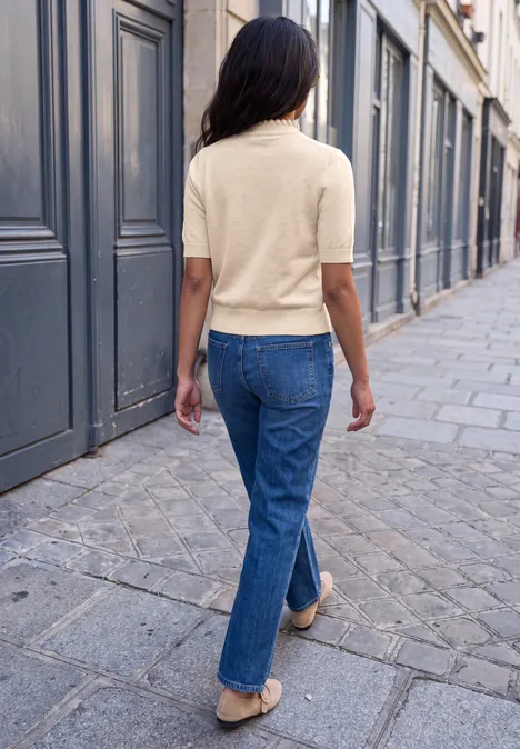 Une femme en jeans et pull à manches courtes marche dans une rue pavée d'une ville.