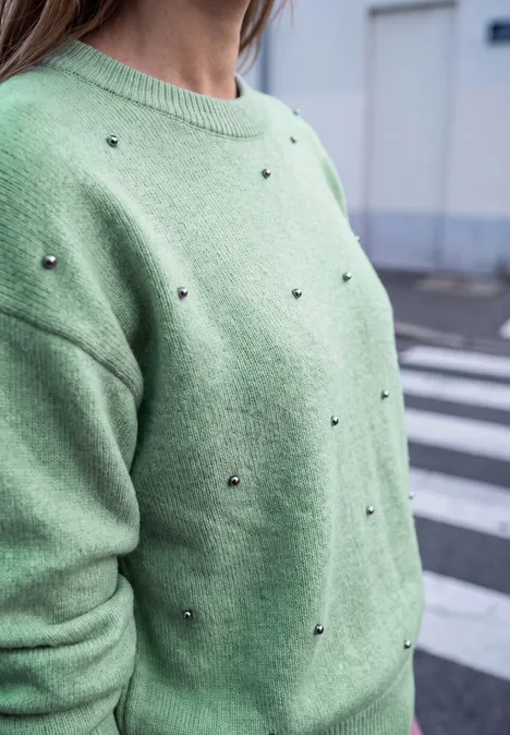 Trui met ronde hals en parelversieringen grayed mint mel. Vrouw in lichtgroene trui met kleine zilveren studs, op straat.