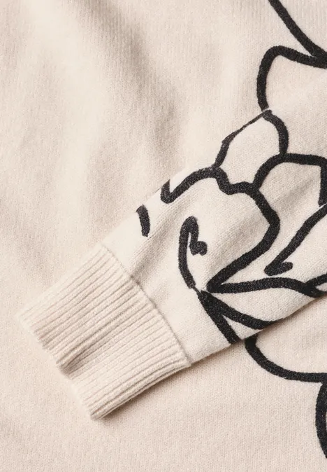 Ärmel eines cremefarbenen Pullovers mit schwarzem, skizzenhaftem Blumenprint.