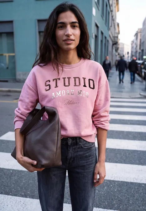 Frau in rosa Sweatshirt und Jeans mit großer Tasche steht auf einem Zebrastreifen in der Stadt.