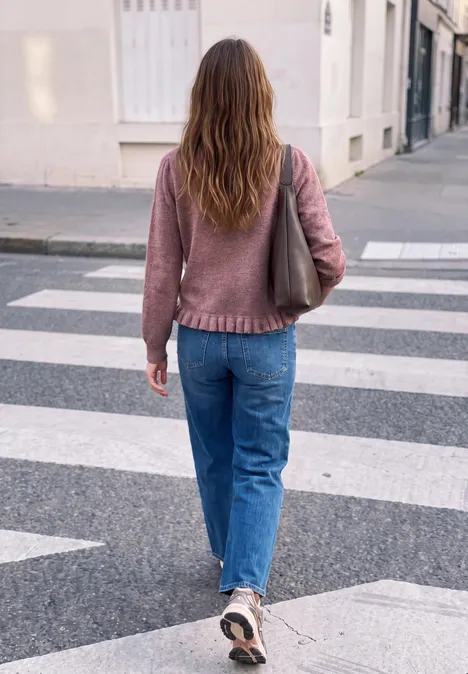 Pullover mit Rundhals und Rüschen am Saum hazy rose mel. Eine Frau mit rosa Pullover, blauen Jeans und Tasche über der Schulter überquert einen Zebrastreifen in der Stadt.