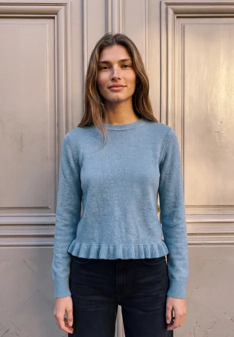 Pullover mit Rundhals und Rüschen am Saum loom blue mel. Eine Frau im blauen Pullover steht vor einer hellen Wand und blickt in die Kamera.