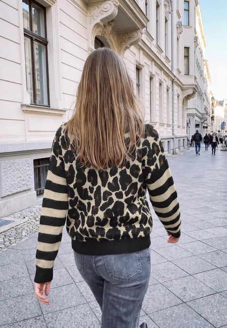 Pull à motif léopard et manches rayées Black Frau mit langem Haar und Leopardenpullover spaziert durch eine elegante, städtische Gasse.