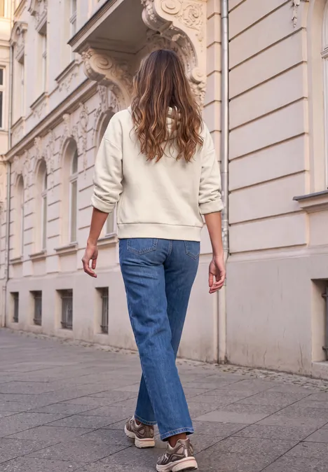 Person in Jeans und Pullover spaziert an alten Stadthäusern entlang.