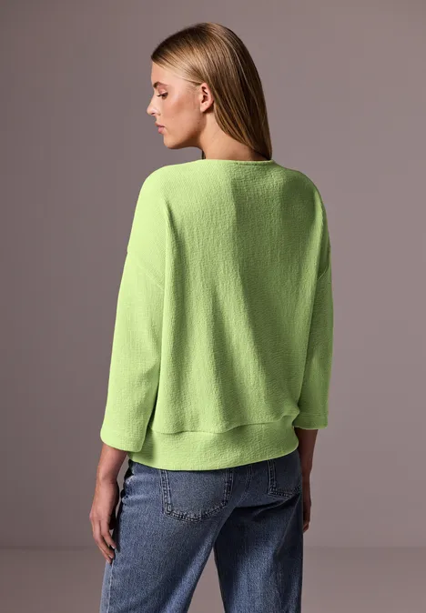 Femme de dos en pull vert clair et jean bleu.