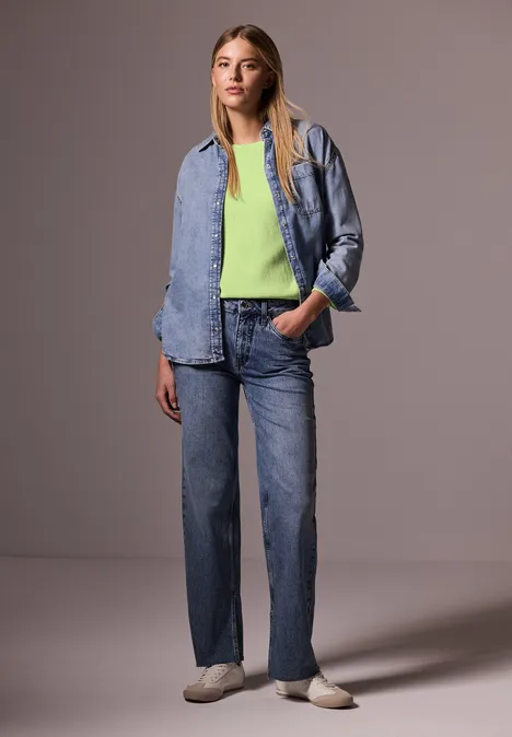 Femme en jean et chemise en jean, haut vert clair, baskets blanches, pose décontractée.