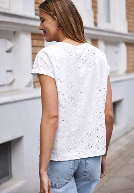 Een vrouw van achteren in een wit ajourshirt en blauwe spijkerbroek op een stoep.
