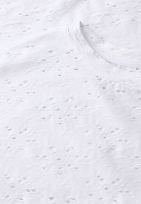 Close-up van wit opengewerkt textiel met fijn, gestructureerd borduurpatroon