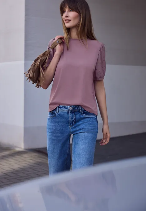 Frau mit rosa Oberteil, blauer Jeans und brauner Fransen-Tasche läuft draußen.