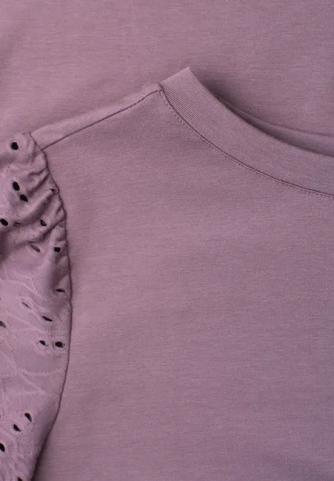 Nahaufnahme eines violetten Shirts mit gerafftem Ärmel und dekorativen Cut-out-Details.