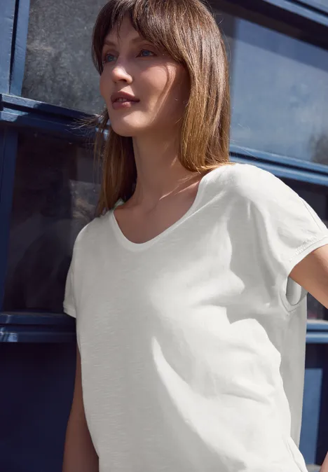 Jonge vrouw in loszittend wit T-shirt voor een blauwe achtergrond.