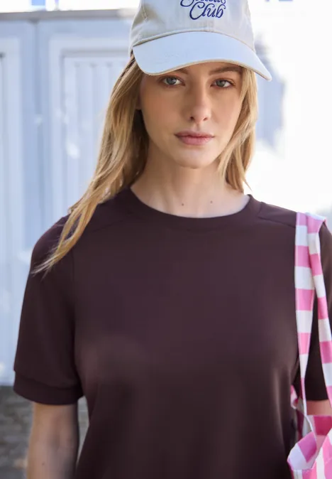 Basic T-Shirt mit Kurzarm und Rundhals very berry Frau mit Basecap und braunem T-Shirt trägt eine pink-karierte Tasche.