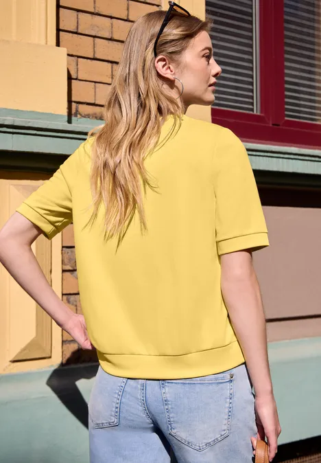 T-shirt basique à manches courtes et col rond null Femme vue de dos portant un t-shirt jaune et un jean devant un mur coloré