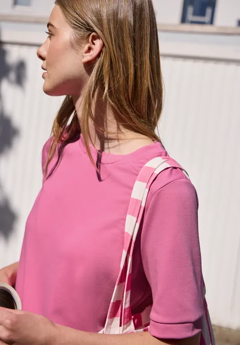Jong meisje opzij gefotografeerd in een roze shirt met een gestreepte tas over haar schouder.