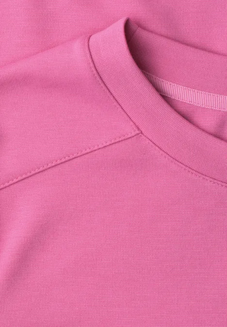 Close-up van een roze sweater met ronde hals en zachte stof.