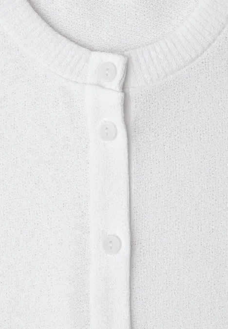 Gros plan d’un cardigan en maille blanc avec boutonnière.