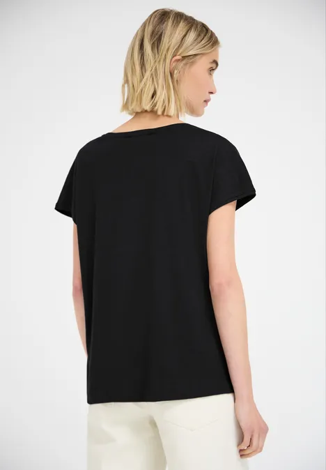 Frau von hinten in schlichtem schwarzem T-Shirt mit kurzen Ärmeln und weißen Hosen.