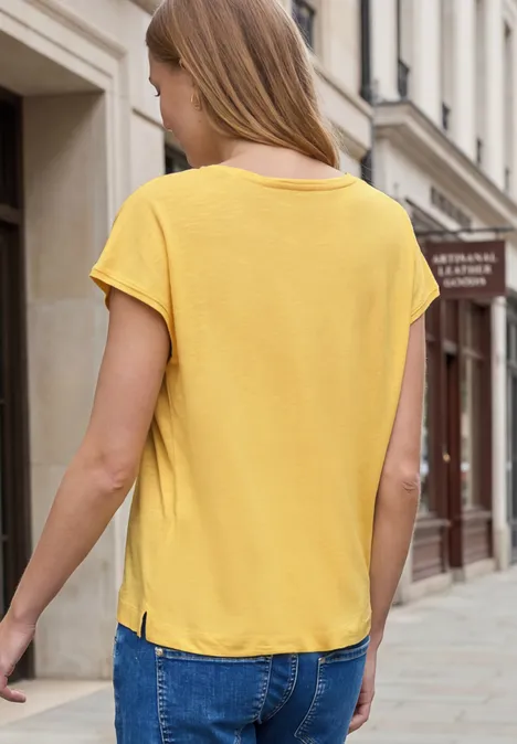 Vrouw in geel shirt loopt door een stadstraat met gevels op de achtergrond.