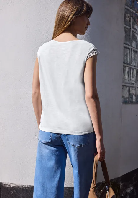 Vrouw van achteren in wit mouwloos topje en blauwe jeans, houdt een tas bij de muurhoek.