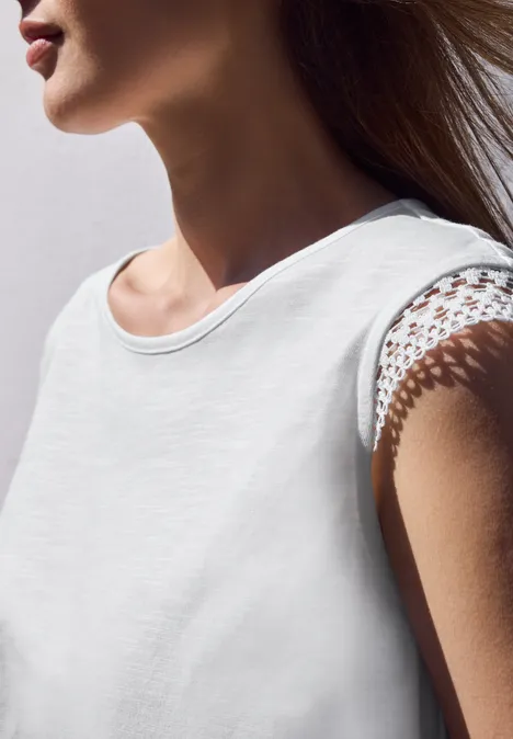 Zijaanzicht van een vrouw in een witte top met kanten mouw.