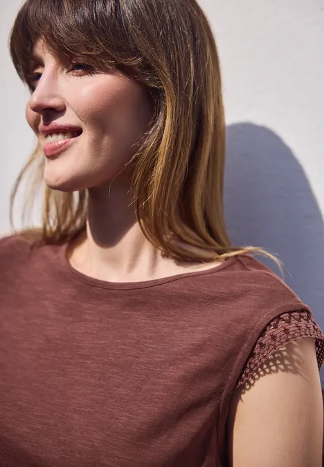 Shirt met ronde hals en gehaakte mouwen mahogany brown Een persoon voor een witte muur draagt een roodbruin T-shirt met netpatroon op de mouw.