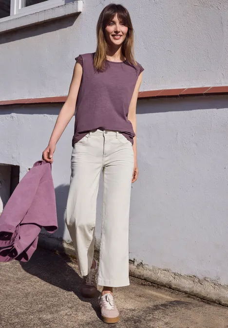 Een persoon in witte broek en paarse top met bijpassend jasje loopt langs een muur buiten.