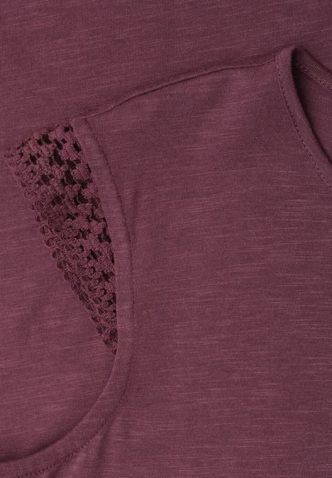 Nahaufnahme eines ärmellosen, bordeauxfarbenen Oberteils mit filigraner Spitzenborte an der Schulter.