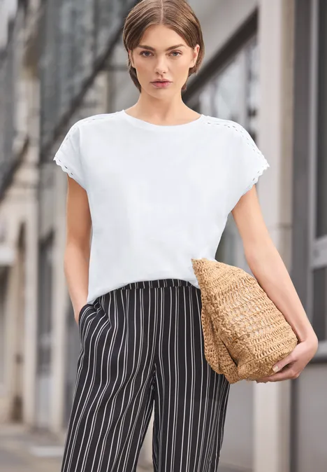 Vrouw in wit T-shirt, zwart-witte gestreepte broek met rieten tas op straat