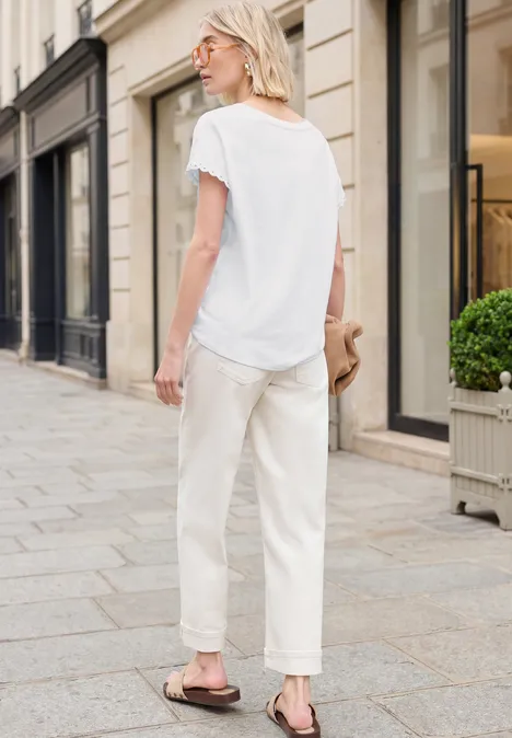 Blonde vrouw van achteren in wit T-shirt en lichte broek, lopend over een geplaveide straat in de stad.