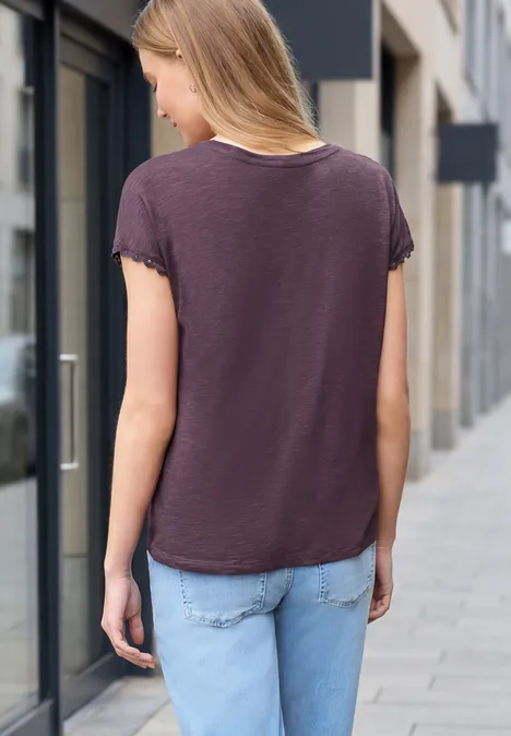 Junge Frau von hinten auf einem Bürgersteig, trägt dunkles T-Shirt und Jeans in urbaner Umgebung.