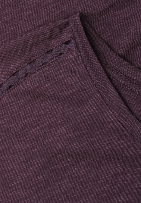 Nahaufnahme eines violetten T-Shirts aus strukturiertem Stoff mit feiner Ziernaht am Ausschnitt.