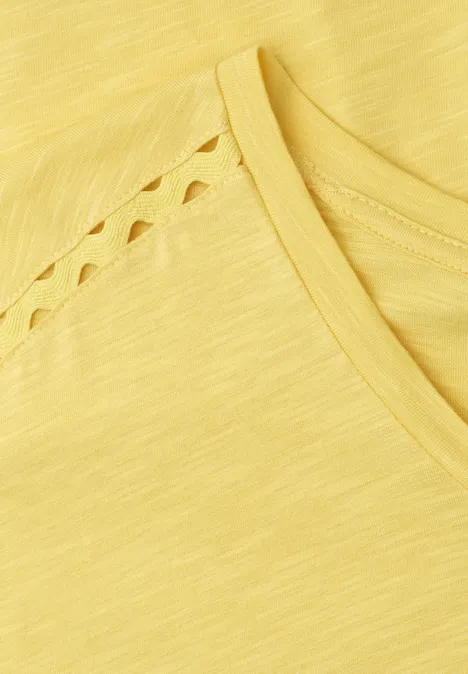 Nahaufnahme eines gelben T-Shirts mit Zierausschnitten an der Schulterpartie.