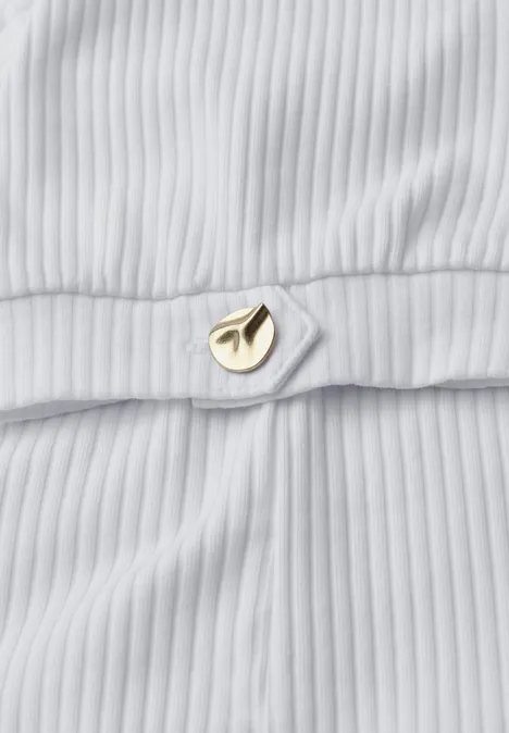 Close-up van geribd wit stof met een klein gouden sierelement.