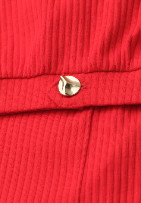 Nahaufnahme eines roten, gerippten Stoffs mit einem kleinen goldfarbenen Metallknopf