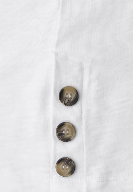 Nahaufnahme eines weißen Stoffes mit drei braunen Knöpfen in vertikaler Anordnung.