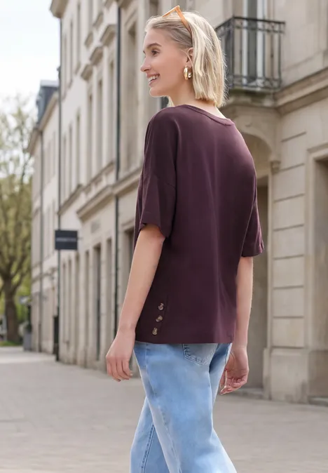 Frau mit blonden Haaren in violettem Kurzarmshirt und blauen Jeans spaziert an klassischer Häuserzeile.