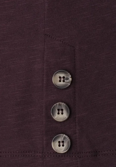 Dunkelviolettes Kleidungsstück mit drei grauen Knöpfen an einer Naht