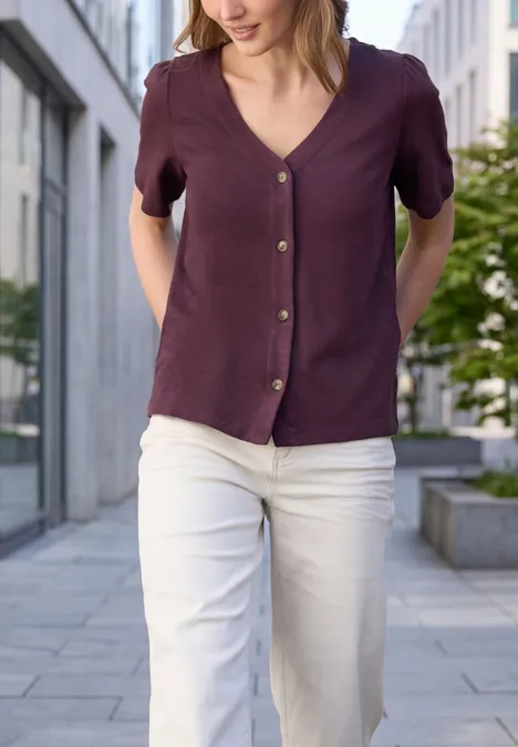 Eine Frau geht in weißer Hose und lila/blauer Bluse durch eine städtische Umgebung.