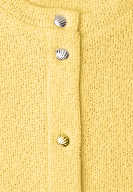 Nahaufnahme eines gelben Strickcardigans mit muschelförmigen Knöpfen in Silber und Gold.