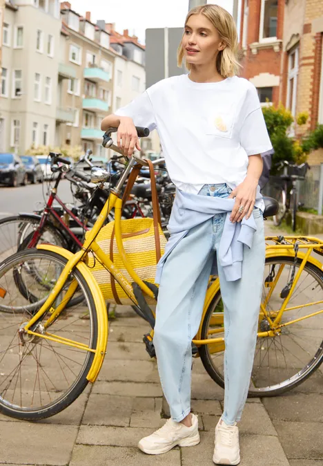 T-Shirt mit Rundhals und Perlendetail White Person steht mit gelbem Fahrrad auf einer städtischen Straße, trägt weißes Shirt und weite Jeans.