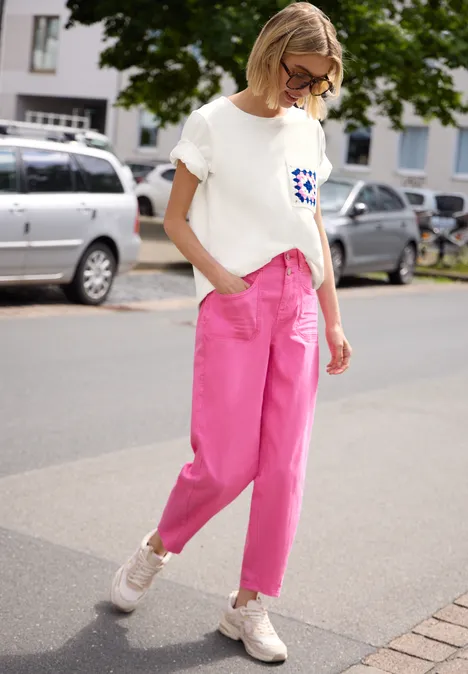 Ein Kind in weißem T-Shirt und pinken Hosen geht vor parkenden Autos auf dem Bürgersteig.