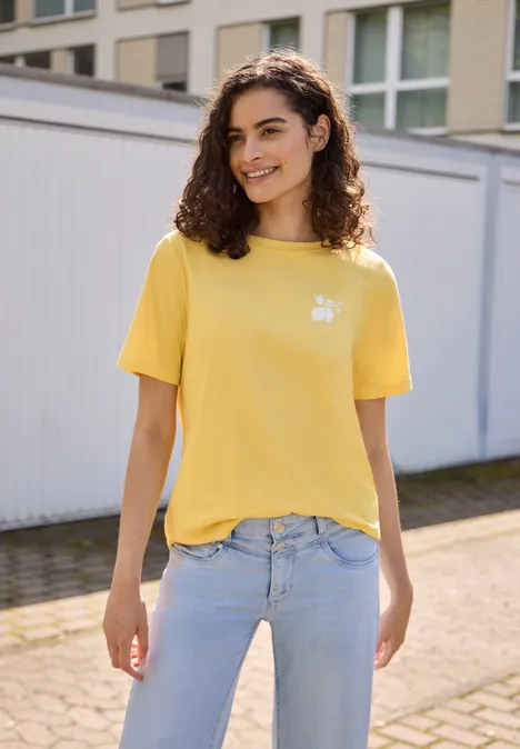 Eine Frau in gelbem T-Shirt und hellblauer Jeans steht vor Garagentoren.