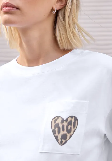 Weißes T-Shirt mit Brusttasche, darauf ein Herz im Leopardenmuster, getragen von Frau mit blondem Kurzhaar.